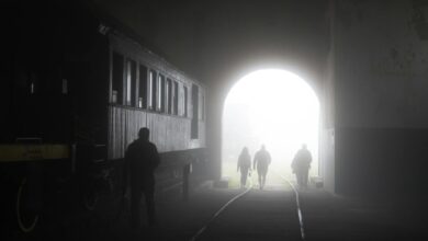 Misty tunnel scene with people walking along train tracks, creating eerie silhouettes.