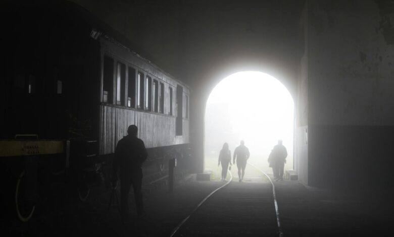 Misty tunnel scene with people walking along train tracks, creating eerie silhouettes.