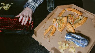 A gamer enjoys pizza and soda in a dimly lit room with a red-lit keyboard.