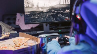 Teen playing video game with headset and drinks, indulging in pizza during gaming session.
