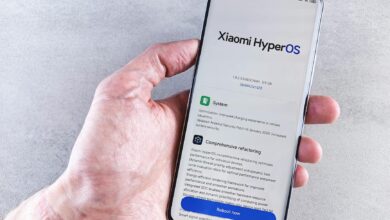 Close-up of a hand holding a Xiaomi smartphone with HyperOS interface, showcasing comprehensive refactoring and system update details.