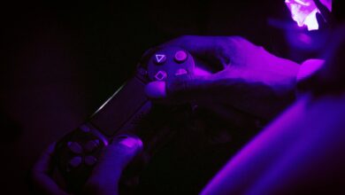 A close-up shot of hands gripping a gaming controller, illuminated by purple light, creating a vibrant atmosphere.