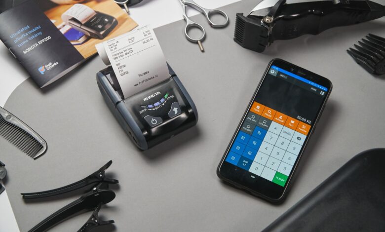 Overhead view of modern black cash register and calculator on smartphone composing with clipper and other tool for cutting hair in barbershop