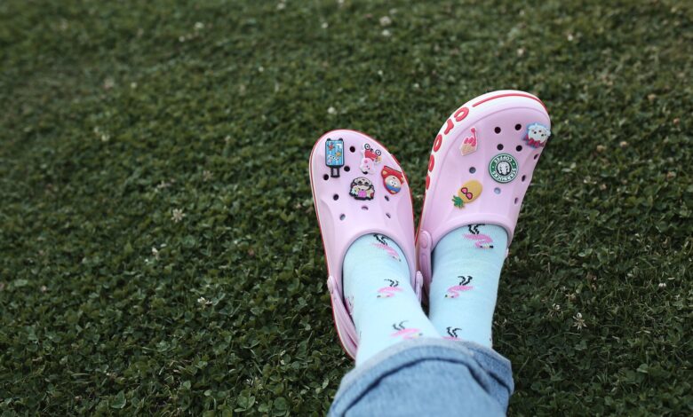 Feet in pink Crocs with playful sock designs resting on grass, depicting leisurely outdoor relaxation.