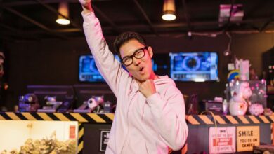 A cheerful gamer in a pink hoodie celebrating victory with a smiling face indoors.