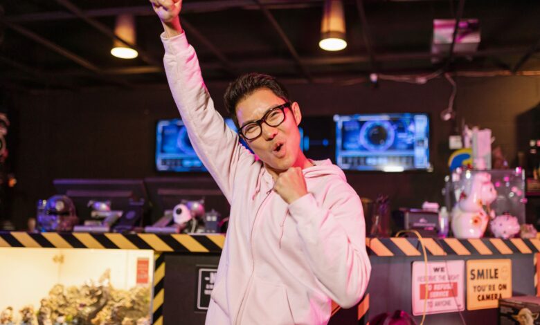 A cheerful gamer in a pink hoodie celebrating victory with a smiling face indoors.