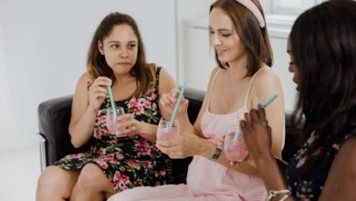 Three women relaxing and enjoying pink drinks on a sofa indoors, capturing a casual and friendly moment.