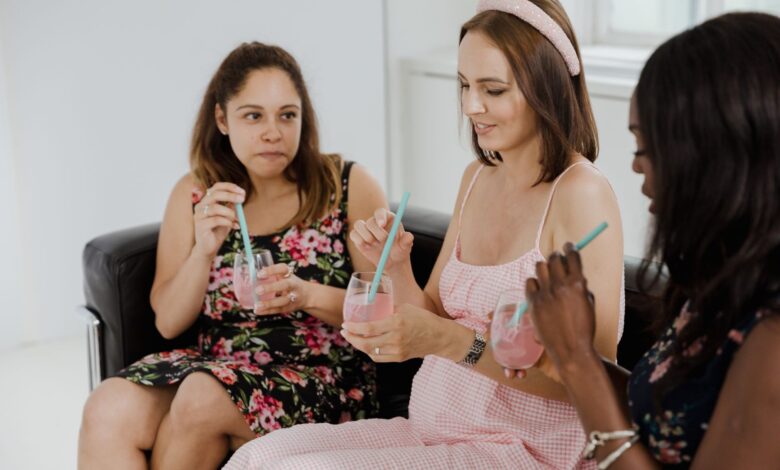Three women relaxing and enjoying pink drinks on a sofa indoors, capturing a casual and friendly moment.