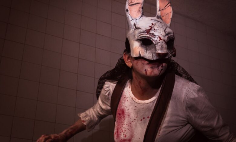 Frightening rabbit mask worn during Halloween with bloodstained costume and eerie lighting.