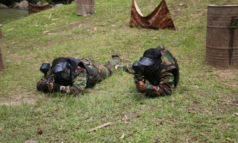 Two adults wearing camouflage gear and masks engaging in a paintball game in an outdoor setting.