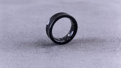 A modern black smart ring with visible circuitry resting on a textured concrete surface.