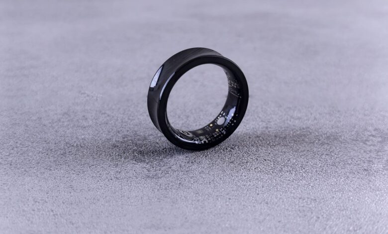 A modern black smart ring with visible circuitry resting on a textured concrete surface.