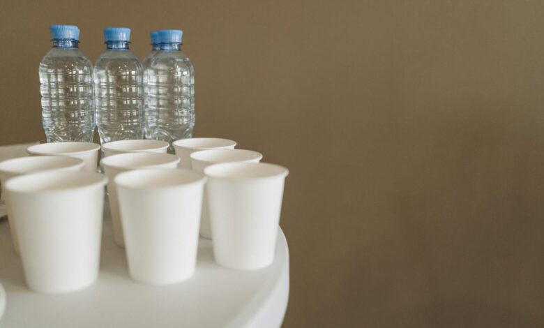Close-up of disposable cups and bottled water with copyspace on a white table.