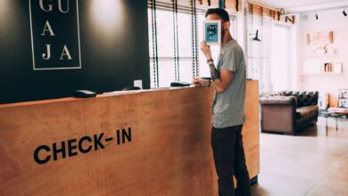 Man standing at a reception desk, holding a book, in a modern hotel lobby.