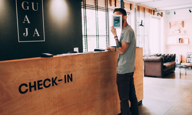 Man standing at a reception desk, holding a book, in a modern hotel lobby.