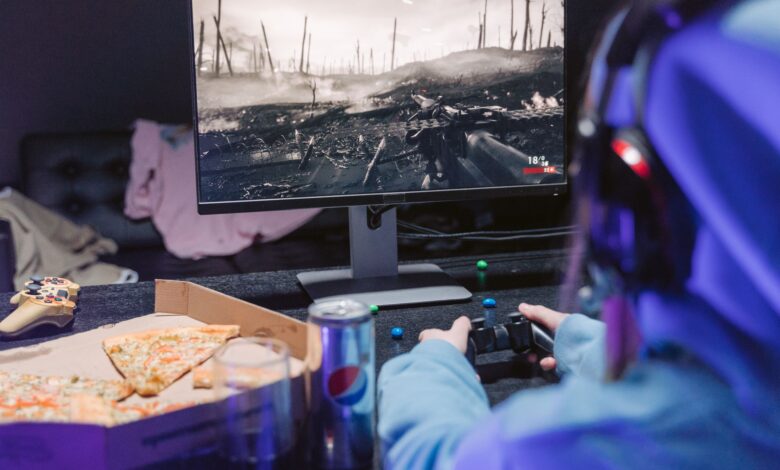 Teen playing video game with headset and drinks, indulging in pizza during gaming session.