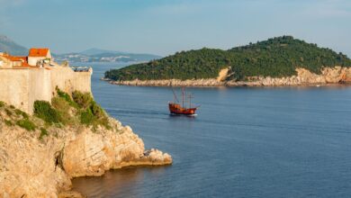 A picturesque view of Dubrovnik's historic coastline with an old ship sailing near a rocky cliff.