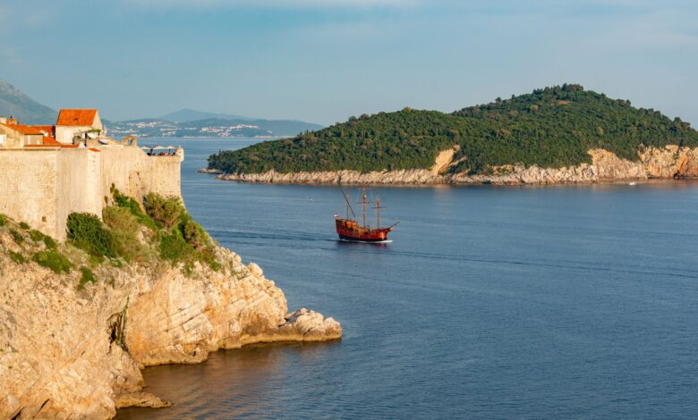 A picturesque view of Dubrovnik's historic coastline with an old ship sailing near a rocky cliff.