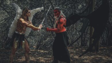 A dramatic cosplay scene of an angel and demon with swords in a forest.