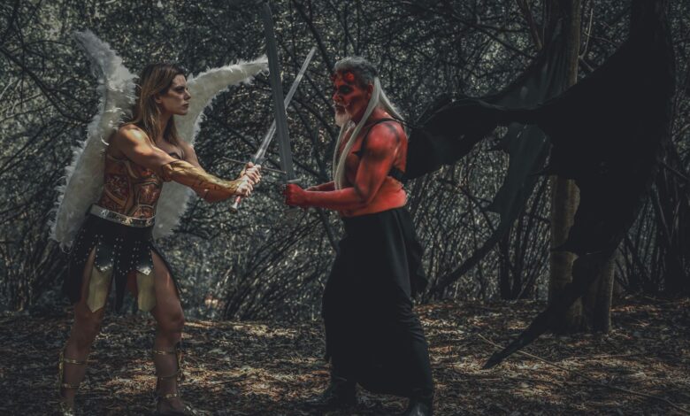 A dramatic cosplay scene of an angel and demon with swords in a forest.