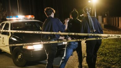 Nighttime arrest scene with police officers and patrol car behind caution tape.