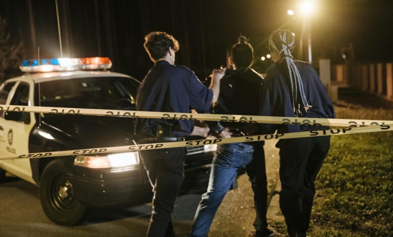 Nighttime arrest scene with police officers and patrol car behind caution tape.