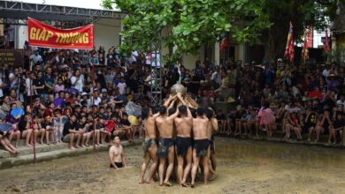 Participants engage in a traditional Vietnamese mud festival, cheered by a large crowd.