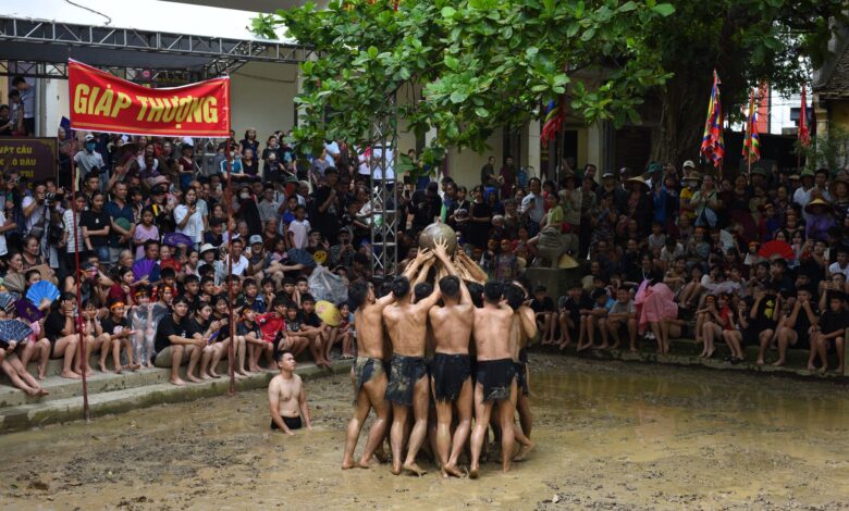 Participants engage in a traditional Vietnamese mud festival, cheered by a large crowd.