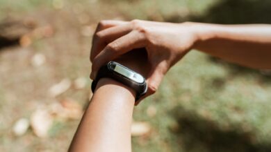 Crop unrecognizable female checking notifications on hand fitness tracker while exercising on green lawn on sunny summer day