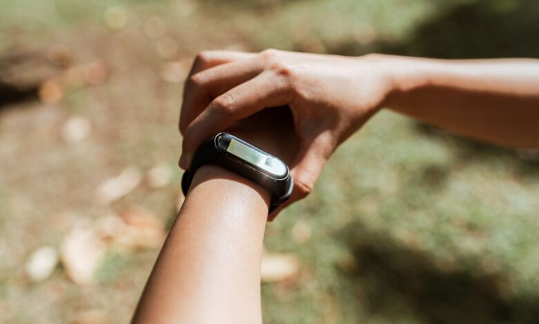 Crop unrecognizable female checking notifications on hand fitness tracker while exercising on green lawn on sunny summer day