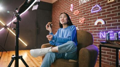 Young Asian woman streaming live indoors with neon lights, engaging audience through technology and creative content.