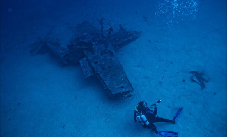 A scuba diver explores a submerged shipwreck deep underwater, capturing adventure and exploration.