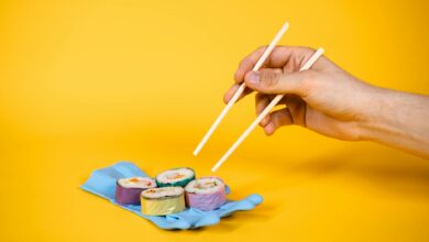 Artistic sushi on a rubber glove with chopsticks, set against a vibrant yellow background.