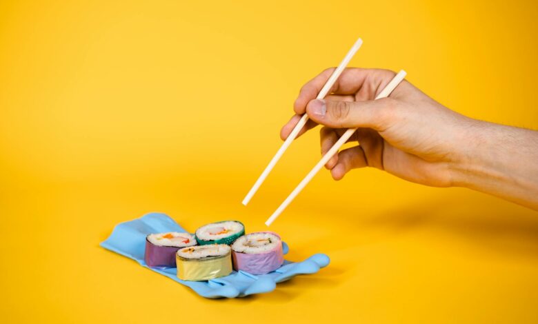 Artistic sushi on a rubber glove with chopsticks, set against a vibrant yellow background.