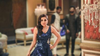 A stylish woman in a blue gown poses elegantly at a luxurious indoor event.