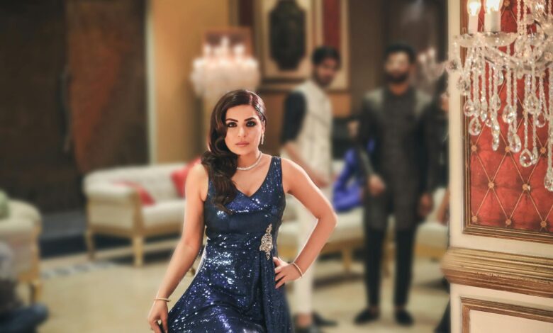 A stylish woman in a blue gown poses elegantly at a luxurious indoor event.
