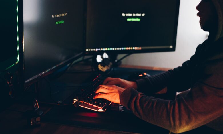 Side view of crop anonymous male cyber thief accessing information on desktop computer screens at dusk