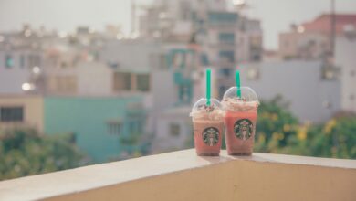 Two Starbucks iced drinks on a sunny balcony with a cityscape background.