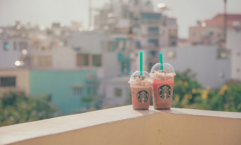 Two Starbucks iced drinks on a sunny balcony with a cityscape background.