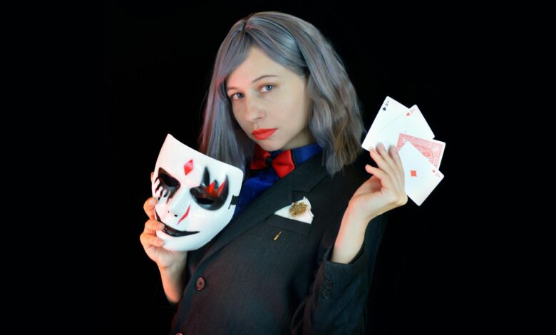 Side view of serious young female casino dealer in classy suit with bow tie holding face mask and cards in hands and looking at camera against black background