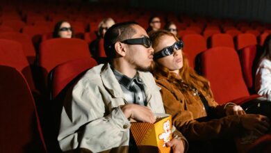 Couple wearing 3D glasses watching a movie in a cinema, enjoying popcorn.