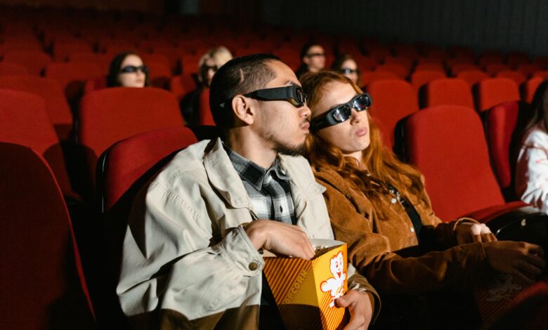 Couple wearing 3D glasses watching a movie in a cinema, enjoying popcorn.