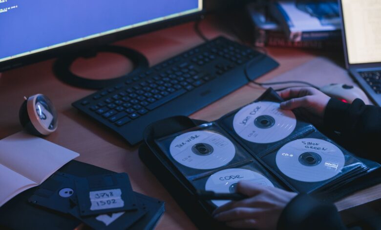 A close-up of CDs and disks on a desk, featuring hands in a tech environment.
