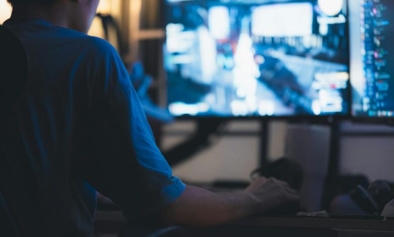 A man intensely focused on a computer screen in a dimly lit room, showcasing concentration in technology.