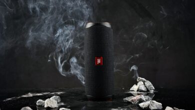 Close-up of a cylindrical speaker on a dark background with smoke and rocks.