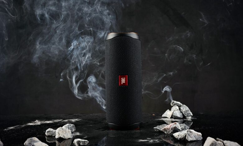 Close-up of a cylindrical speaker on a dark background with smoke and rocks.