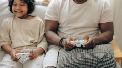 Crop black man and son in sleepwear playing video games on console with joysticks while spending time at home together