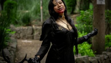 Woman in dark Halloween costume with fake blood in a garden setting, Mexico.