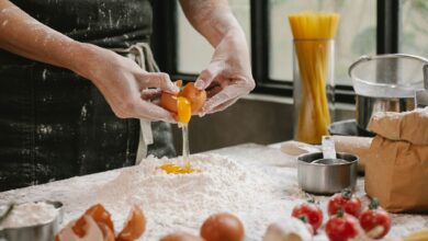 Crop anonymous person adding egg in flour while cooking pastry for recipe with cherry tomatoes and spaghetti