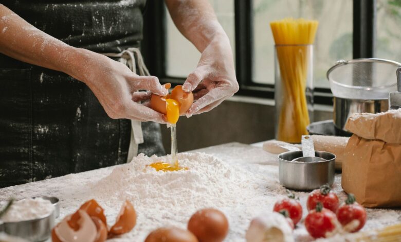 Crop anonymous person adding egg in flour while cooking pastry for recipe with cherry tomatoes and spaghetti